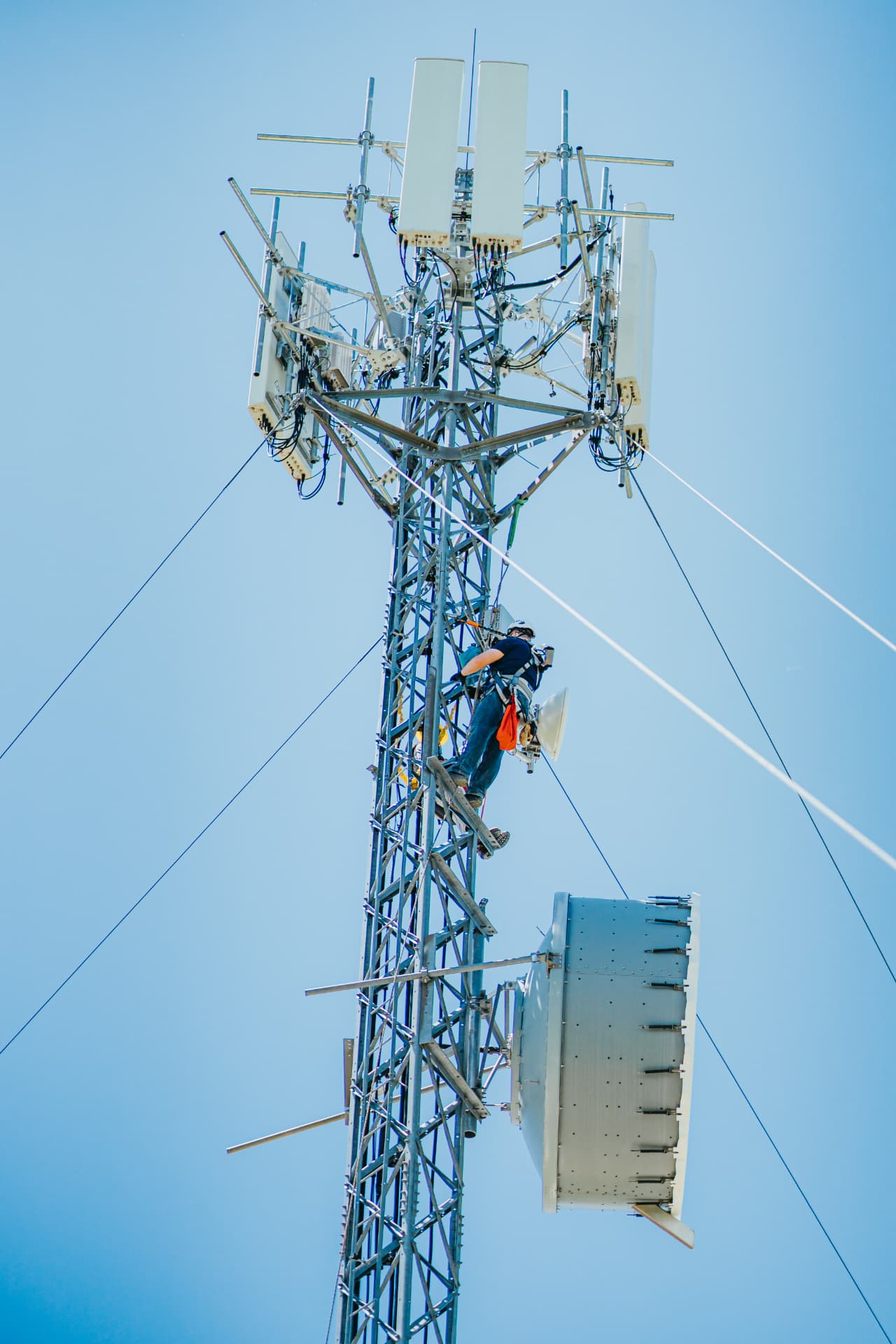 A technician in a safety harness working on antennas near the top of a communications tower