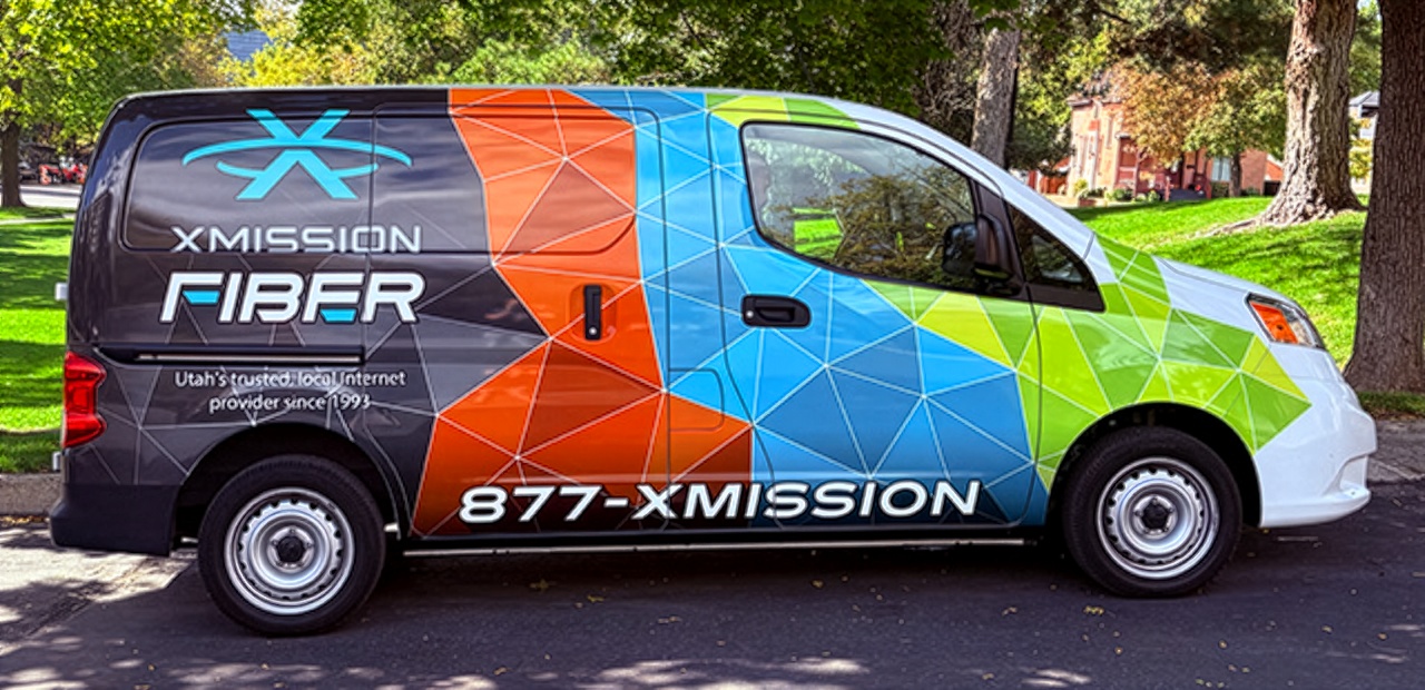 An XMission Fiber service van parked on a tree lined residential street
